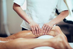 Massage therapist working with patient, massaging his calves. Toned image.