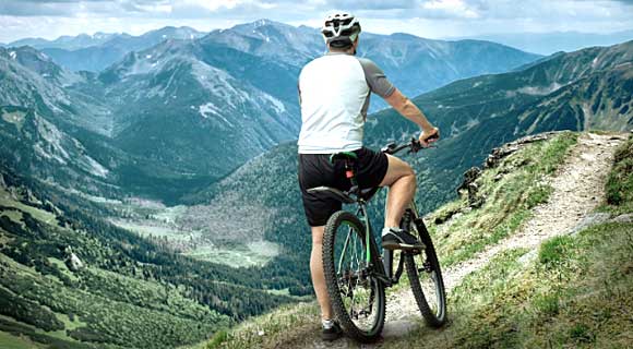 An Adventurous Racer Standing With His Bicycle In A Mountain Peak